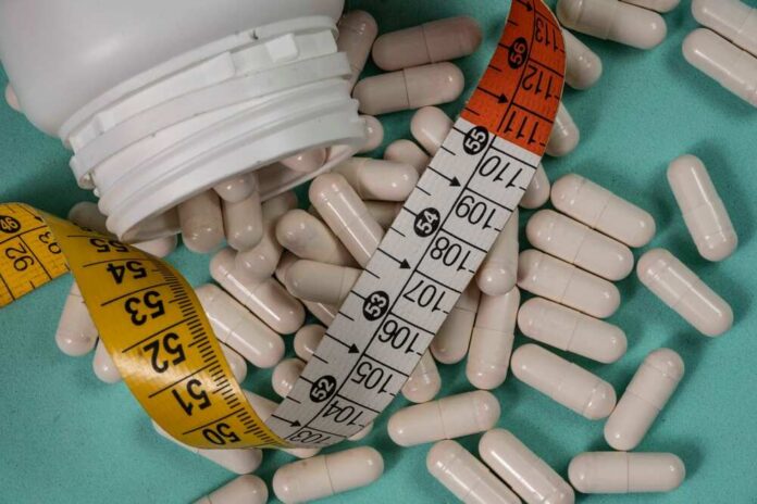 White capsules scattered around a measuring tape and a bottle