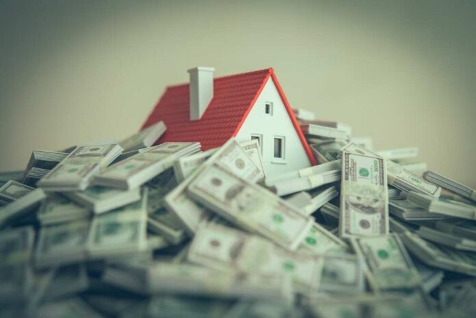 shutterstock_2620353749.jpg A small model house surrounded by stacks of money