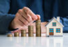 Property Costs Trigger Nationwide Nightmare Hand stacking coins beside a miniature house model.