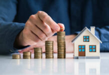 Property Costs Trigger Nationwide Nightmare Hand stacking coins beside a miniature house model.