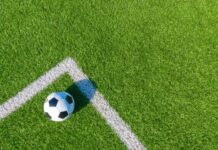A soccer ball resting on a green artificial turf field near the corner