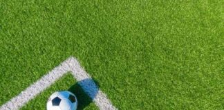 A soccer ball resting on a green artificial turf field near the corner