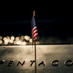 Pentagon Pulls Troops — Who’s Steering the Ship? American flag above engraved Pentagon sign at night