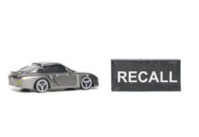 Recall Shocker: Engine Fail Risk! A miniature gray sports car next to a black sign that reads 'RECALL'