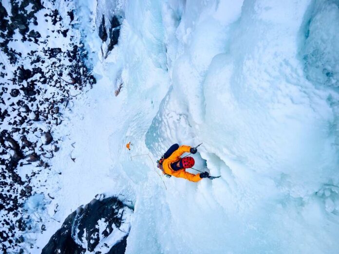 shutterstock_2437128937.jpg A climber ascending a frozen ice wall in a snowy landscape
