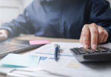 Water Bills EXPLODE — Families Can’t Afford Person using a calculator while working on a laptop and reviewing documents