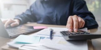 Person using a calculator while working on a laptop and reviewing documents