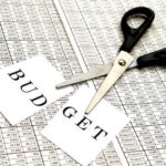 Budget Chaos FREEZES Army Training Scissors cutting a paper labeled 'BUDGET' on a financial spreadsheet
