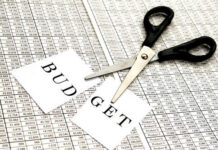 Scissors cutting a paper labeled 'BUDGET' on a financial spreadsheet