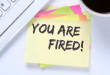 Tech Workers Build AI — Then Get FIRED A sticky note with the message 'YOU ARE FIRED' placed on a desk next to a keyboard and a cup of coffee