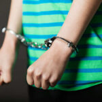 Teenage Killer ARRESTED — Killed 2 Inside Bank Person in striped shirt wearing handcuffs.