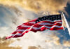 New Boss Takes United States Spy Helm American flag waving against a cloudy sky.