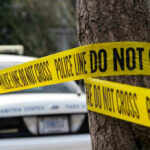 Family Slaughtered – Community Stunned Police tape surrounding a tree and police car.