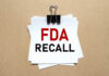 A notice labeled 'FDA RECALL' clipped to white papers on a brown background