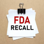 One Word Triggers Federal Recall A notice labeled 'FDA RECALL' clipped to white papers on a brown background