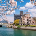 Vanished In Kyoto — Then Found Dead View of the Hiroshima Peace Memorial with cherry blossoms in the foreground