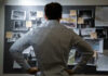 Man examining investigation board with photos and notes.