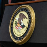 Trump Threatens States: Cut the Cash, Stop the Scams Department of Justice seal on a podium.