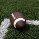Shocking NFL Loss – Dead at 36 A brown football resting on green artificial turf near a white line
