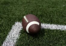 Shocking NFL Loss – Dead at 36 A brown football resting on green artificial turf near a white line