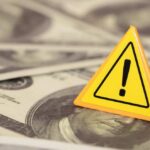 Debt Bomb Ticks — 2008 Vibes Return A yellow warning sign on a background of dollar bills