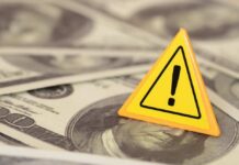 A yellow warning sign on a background of dollar bills