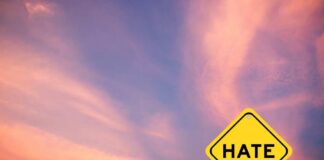 Yellow warning sign with the word HATE against a colorful sunset sky
