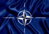 NATO flag with white compass emblem on blue background.