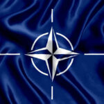 Russian Buzz Job Rattles NATO Nerves NATO flag with white compass emblem on blue background.