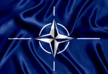 Russian Buzz Job Rattles NATO Nerves NATO flag with white compass emblem on blue background.