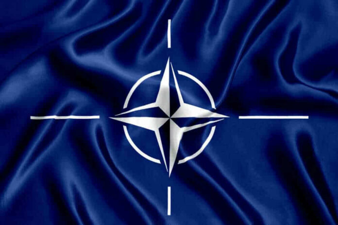 shutterstock_1128305351-1 NATO flag with white compass emblem on blue background.