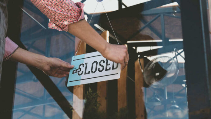 shutterstock_1162554778 Person flipping closed sign on glass door