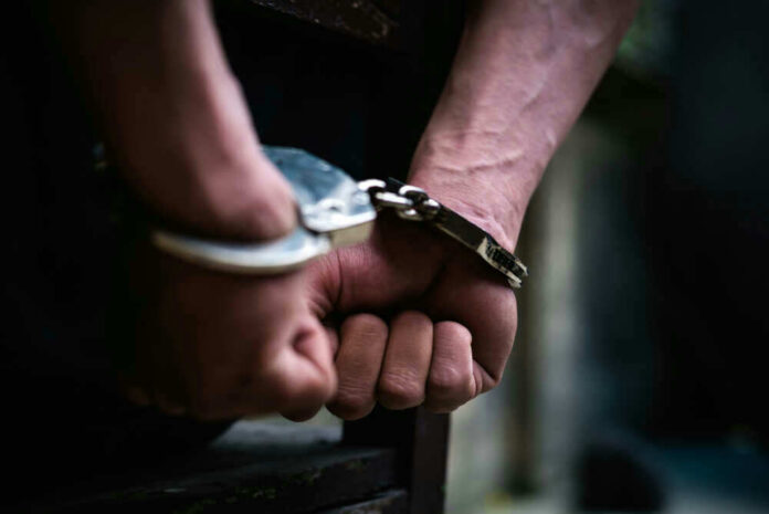 shutterstock_1338116366 Close-up of hands in handcuffs behind back.