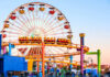 Upside-Down Launch At 100 MPH? Colorful amusement park scene featuring a ferris wheel and roller coaster at sunset