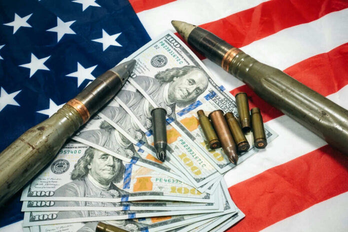 shutterstock_2187827705 American flag with money bullets and weapons on top