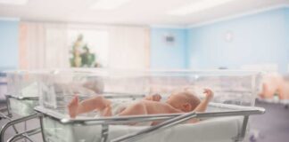 Newborn baby lying in a transparent crib in a hospital nursery
