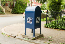 Stamp Shock Hits Sunday Blue USPS mailbox on a residential street corner.
