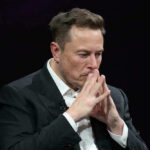Bezos vs. Musk: Space Phone Showdown Elon Musk in a suit deep in thought, black background.