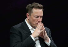 Bezos vs. Musk: Space Phone Showdown Elon Musk in a suit deep in thought, black background.
