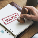 CASE SOLVED: Garage Floor Grave Shocks Community A hand applying a stamp marked 'SOLVED' on a notebook