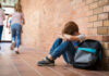 Kids Dosed Daily — CDC Sounds Alarm Sad child sitting against brick wall, kids running away.