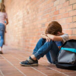 Kids Dosed Daily — CDC Sounds Alarm Sad child sitting against brick wall, kids running away.