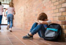Kids Dosed Daily — CDC Sounds Alarm Sad child sitting against brick wall, kids running away.