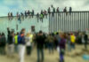 People sit atop a border wall during protest.