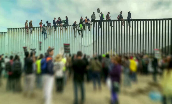 shutterstock_1229072281 People sit atop a border wall during protest.