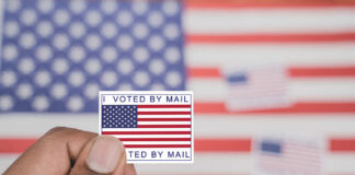 Hand holding a vote-by-mail sticker with U.S. flag