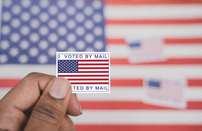 Holding,I,Voted,My,Mail,Sticker,In,Hands,With,Us Hand holding a vote-by-mail sticker with U.S. flag