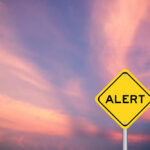 Mystery Outbreak Claims Two Yellow alert sign against a colorful sunset sky