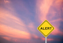 Mystery Outbreak Claims Two Yellow alert sign against a colorful sunset sky