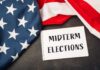 Musk’s Nine-Figure Midterm Gambit American flag and a notebook with 'MIDTERM ELECTIONS' written on it